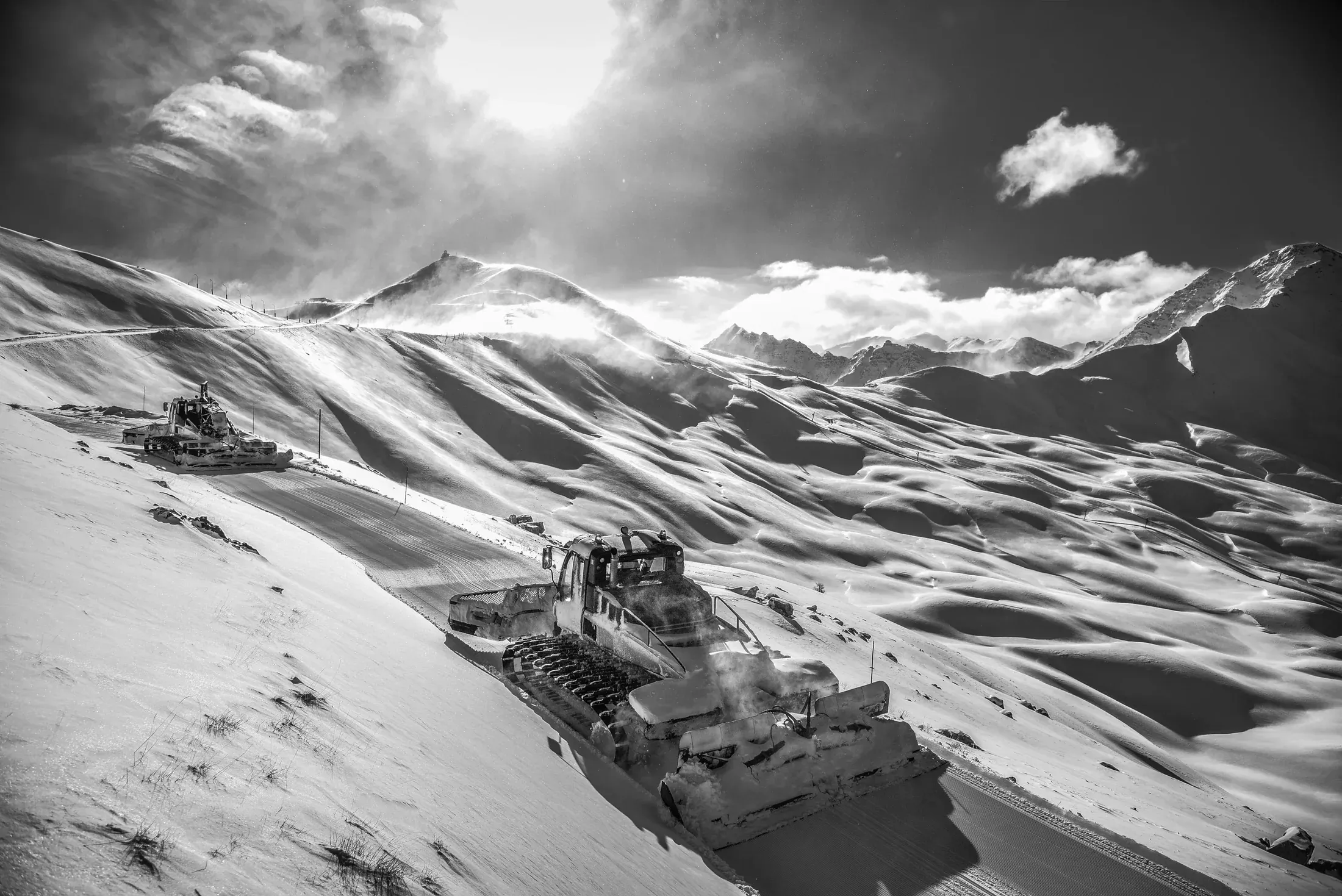 Dameuses au travail sur les pistes d'Ancelle en contre-jour, photographie en noir et blanc