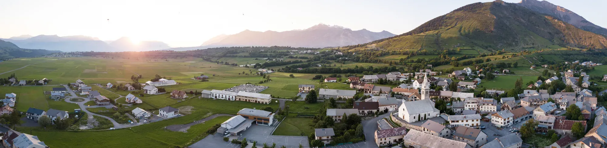 Panorama sur le plateau du Champsaur en été : prés, hameaux et village d'Ancelle au pied de la montagne