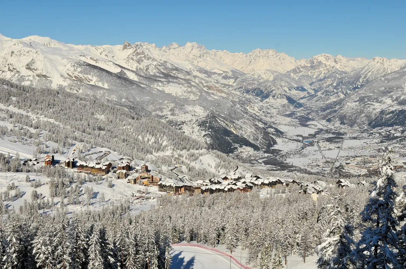 Panorama hivernal sur la station d'Ancelle et la vallée du Champsaur, chalets enneigés et forêt de mélèzes