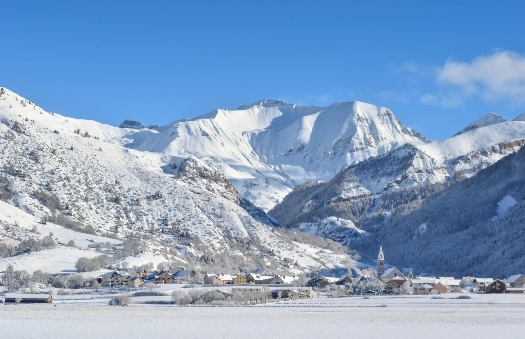 Ancelle sous la neige en hiver, le village au pied des sommets enneigés du Champsaur par ciel bleu